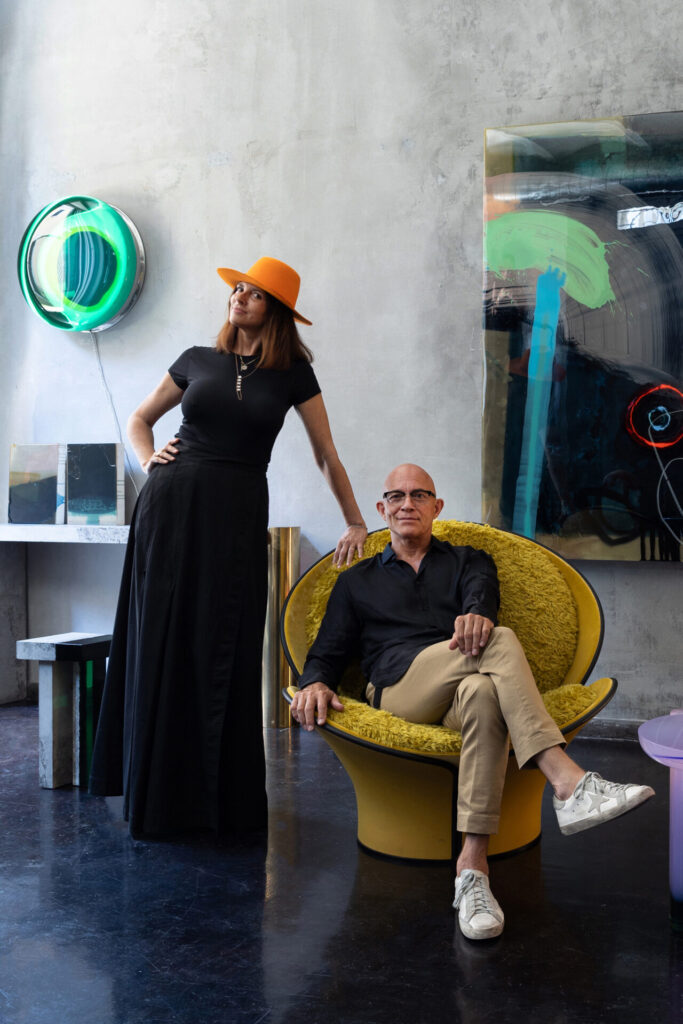 Designers seated in a studio surrounded by sculptural glass lighting and Murano glass objects, highlighting colorful, experimental forms and finishes
