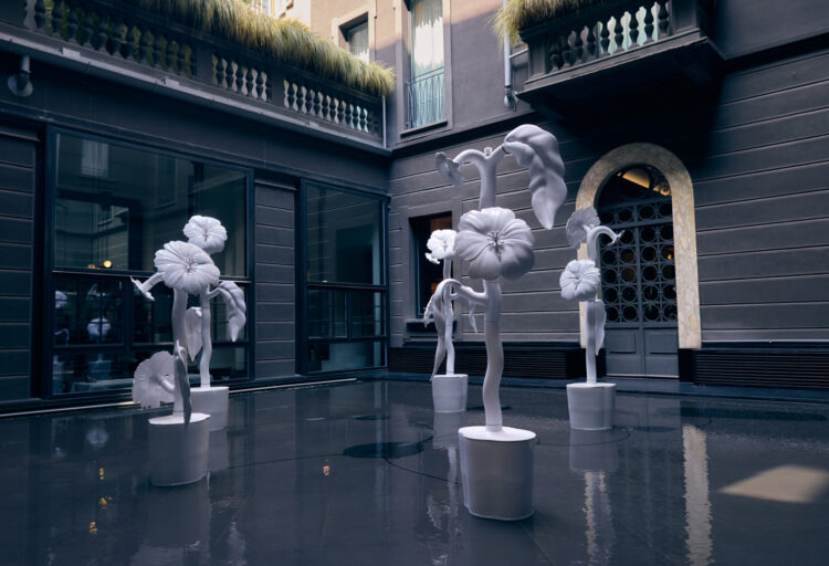 Towering white ceramic flower sculptures rise from reflective water in a courtyard, forming a surreal ceramic sculpture garden installation
