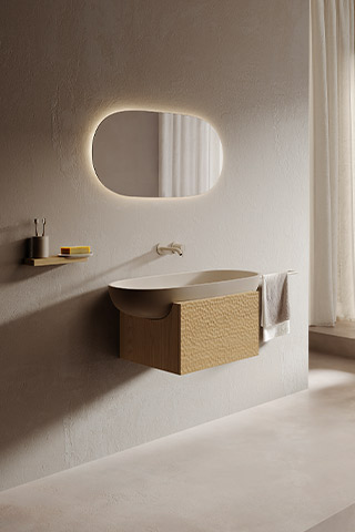 Floating vanity from a sculptural bathroom collection, combining a smooth basin with a textured stone base and warm ambient lighting.