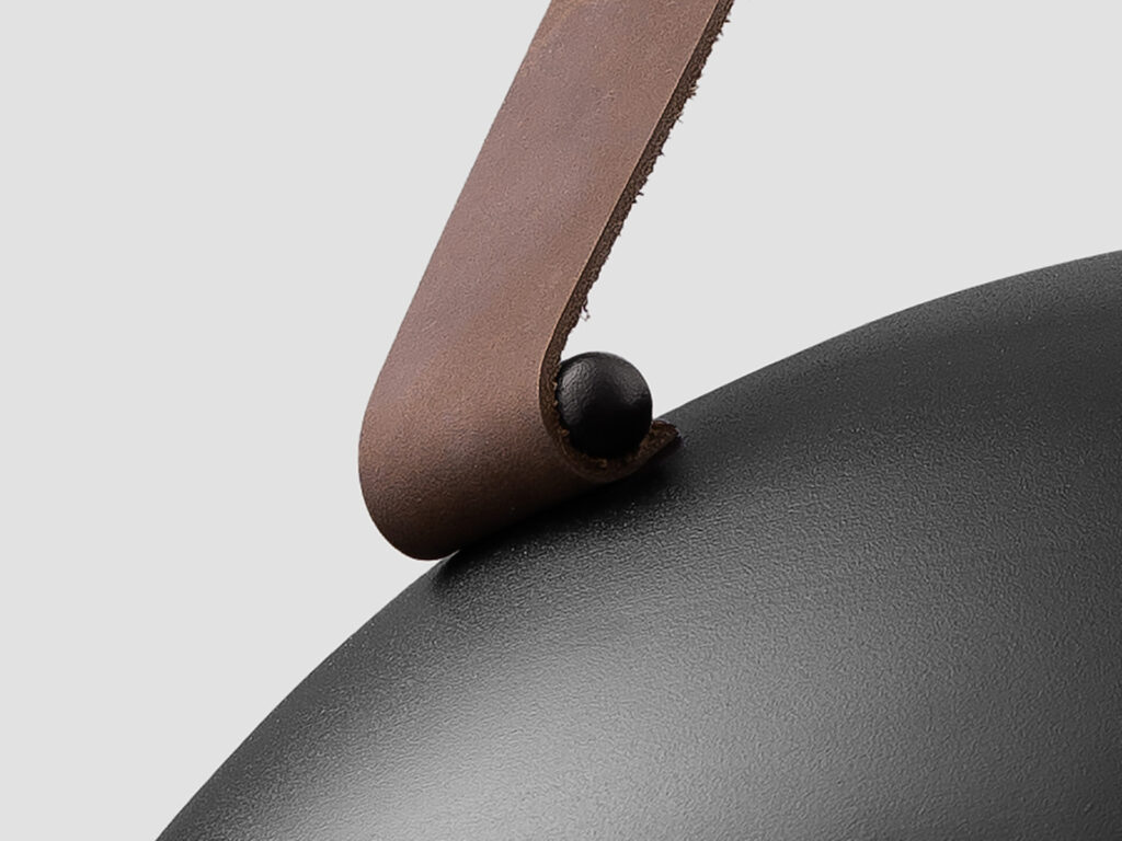 Decorative pendant lighting close-up of leather strap connection with brass hardware against matte metal shade, emphasizing material contrast