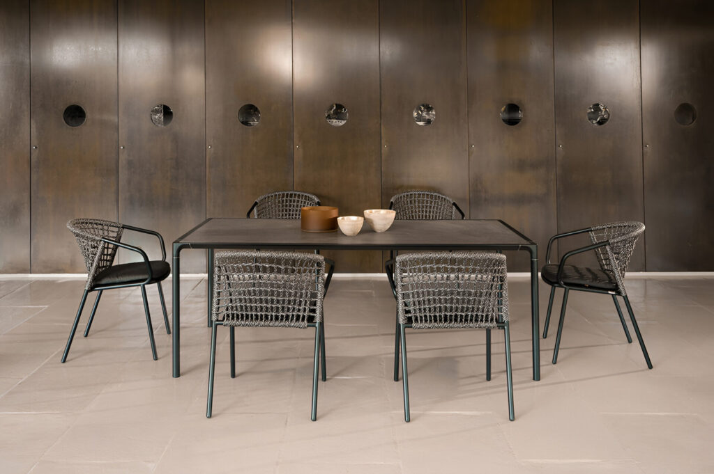 Italian-designed commercial outdoor dining set with woven rope chairs and matte black table positioned against a dark bronze architectural wall for refined hospitality interiors.