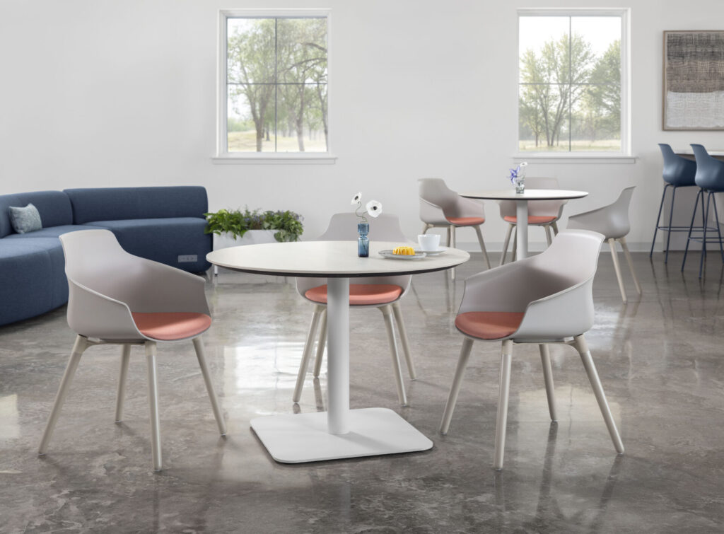 White HON Brim polyshell bucket chairs with blush upholstered seat pads arranged around café tables in a hospitality-inspired workplace setting.