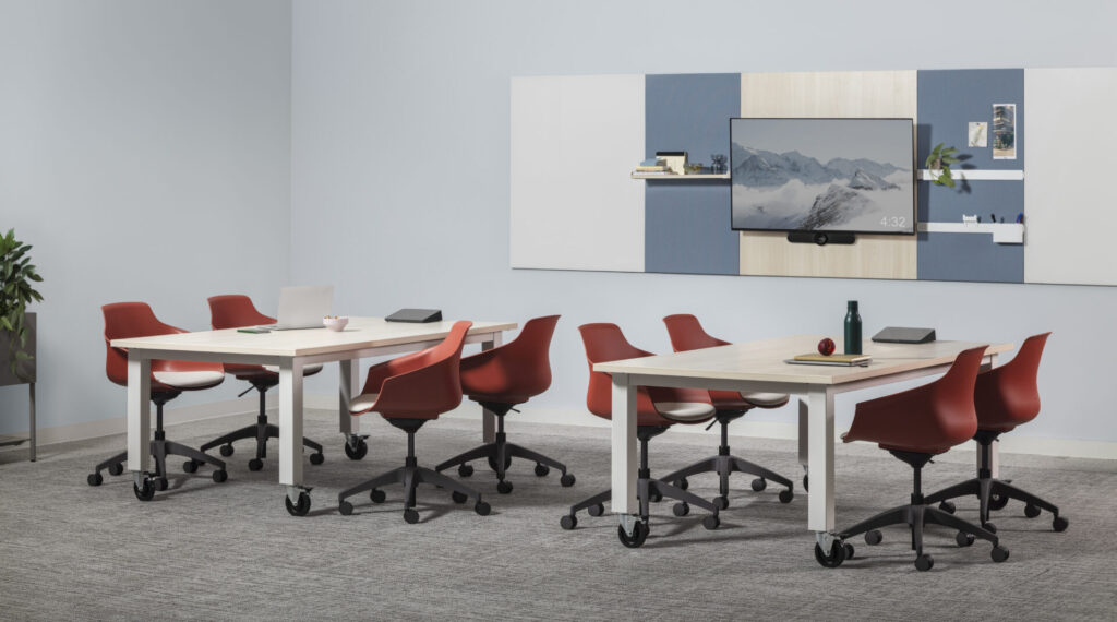 Red HON Brim polyshell bucket chairs gathered around mobile meeting tables in a flexible workplace conference room with integrated AV wall.