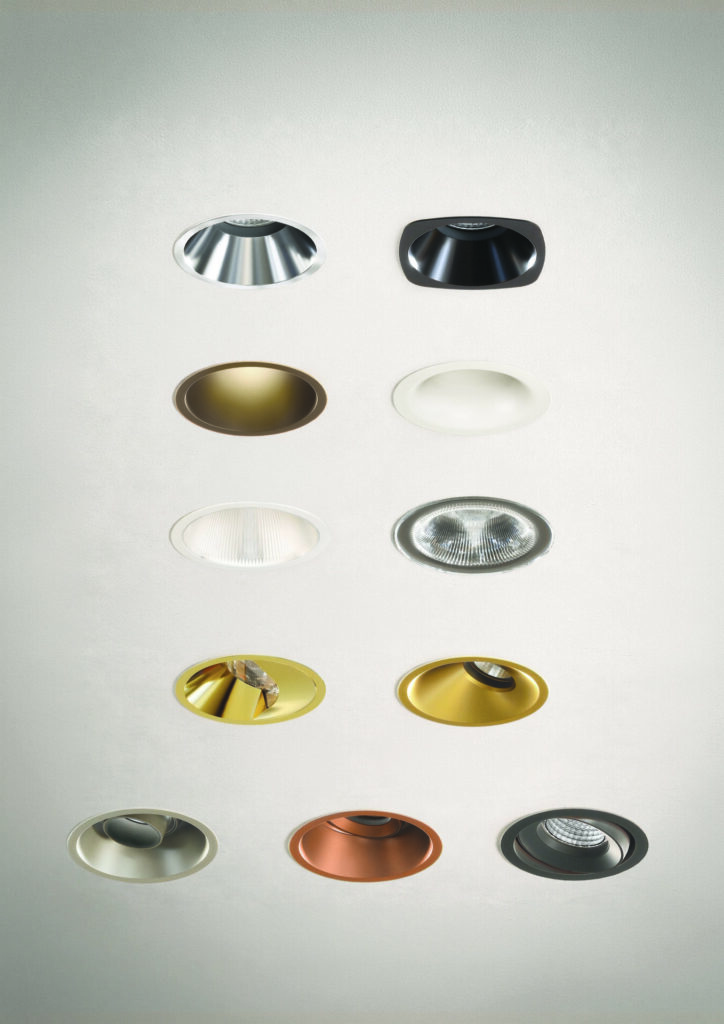 Assorted recessed downlight trims in varied shapes, finishes, and optics displayed on white ceiling surface—modular LED downlight system with customizable apertures