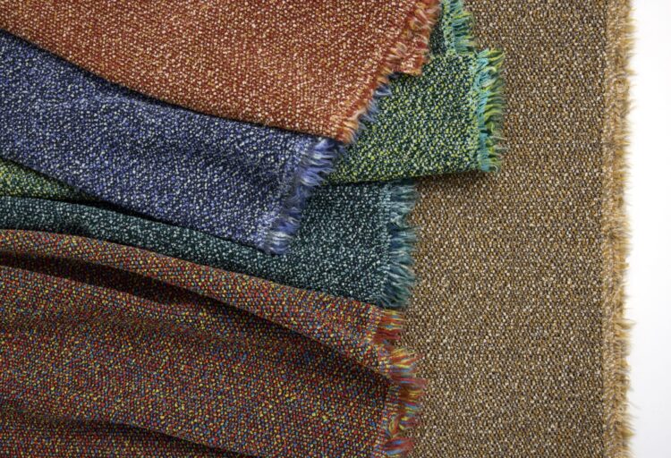 Close-up of layered Luum Textiles upholstery fabrics with richly speckled weaves and frayed edges, highlighting the dimensional texture of Roam performance textiles.