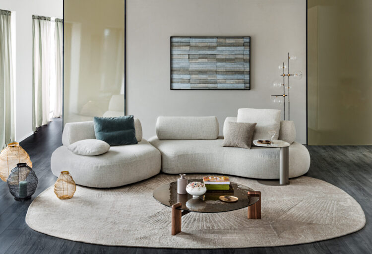 Curved modular sofa in textured ivory upholstery anchors a minimalist living room, paired with sculptural tables and layered neutral textiles for hospitality-inspired lounge seating.