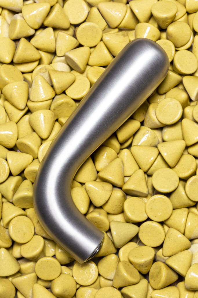 Curved minimalist door handle in brushed aluminum from Verum’s SERIE 85 collection, displayed atop glossy yellow geometric stones.