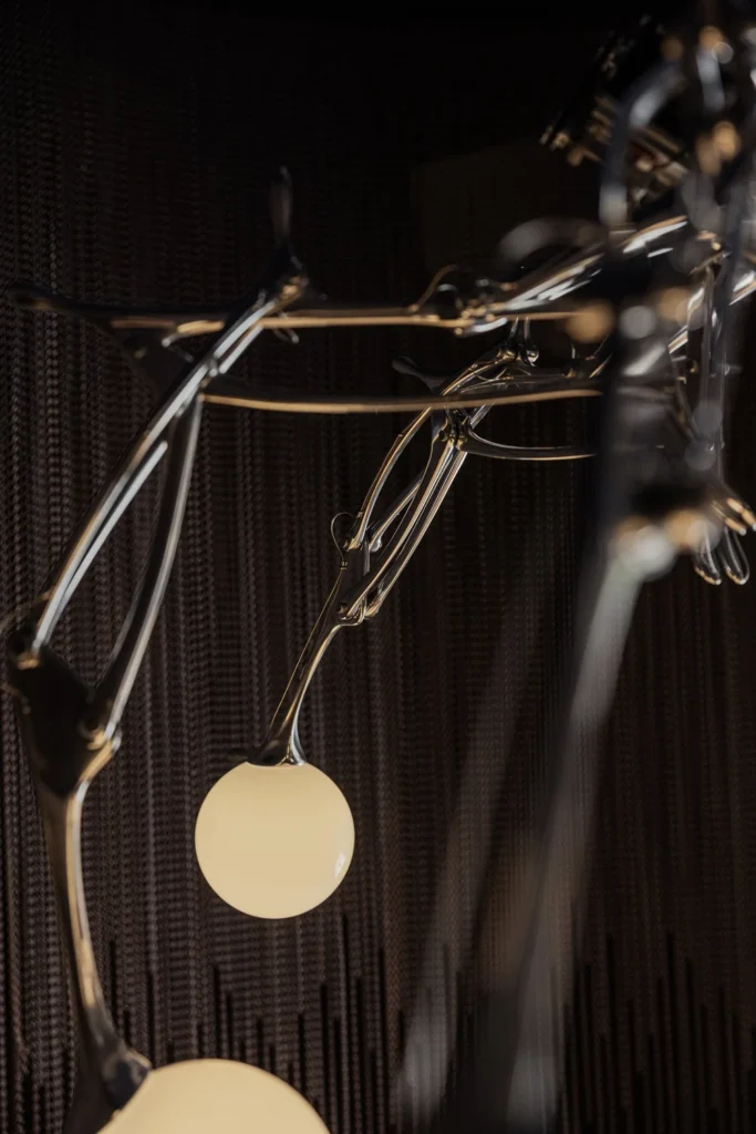 Detailed view of LUMIAC's polished aluminum framework and illuminated glass sphere, showcasing the mechanical elegance of Andrea Mancuso Studio's kinetic chandelier.