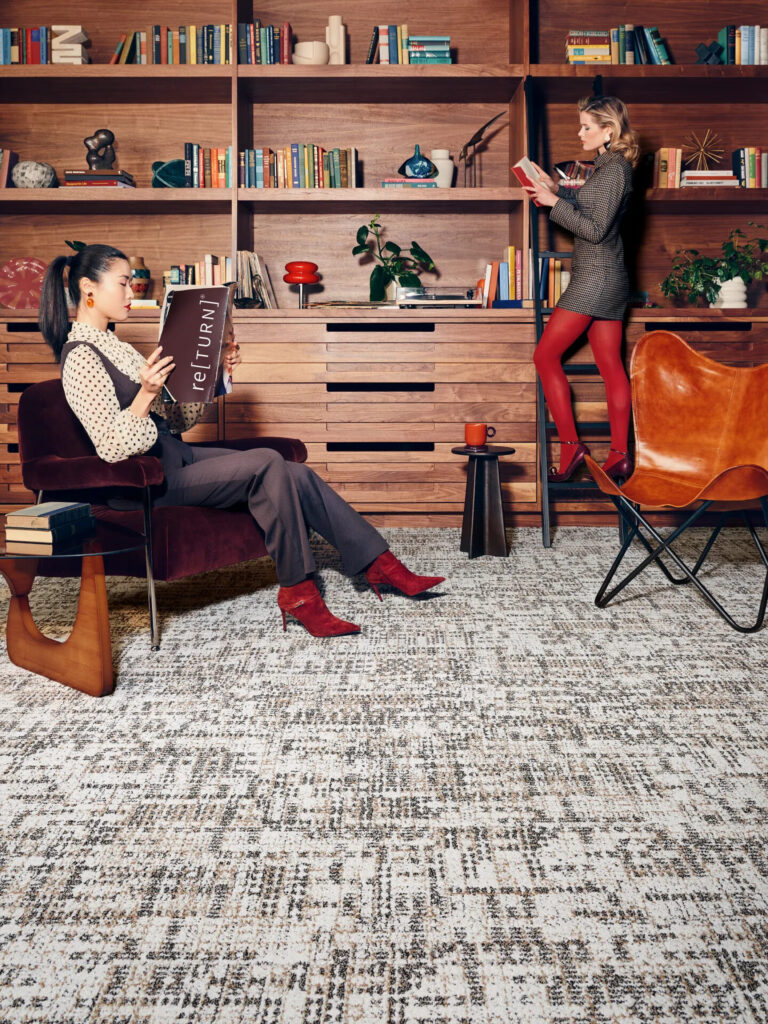 Cult Classics commercial carpet tile by Shaw Contract installed in a library lounge with textured neutral pattern, wood shelving, and contemporary furnishings.