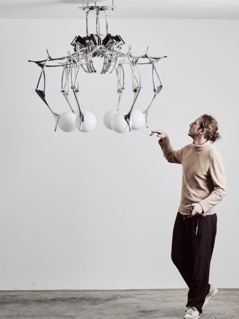 Andrea Mancuso stands beneath the LUMIAC kinetic chandelier, highlighting the fixture's sculptural scale and moving aluminum arms.