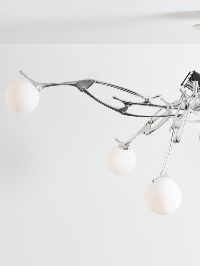 Close-up of LUMIAC's articulated aluminum arm extending outward with glowing blown-glass globes, highlighting the fixture's kinetic lighting design.