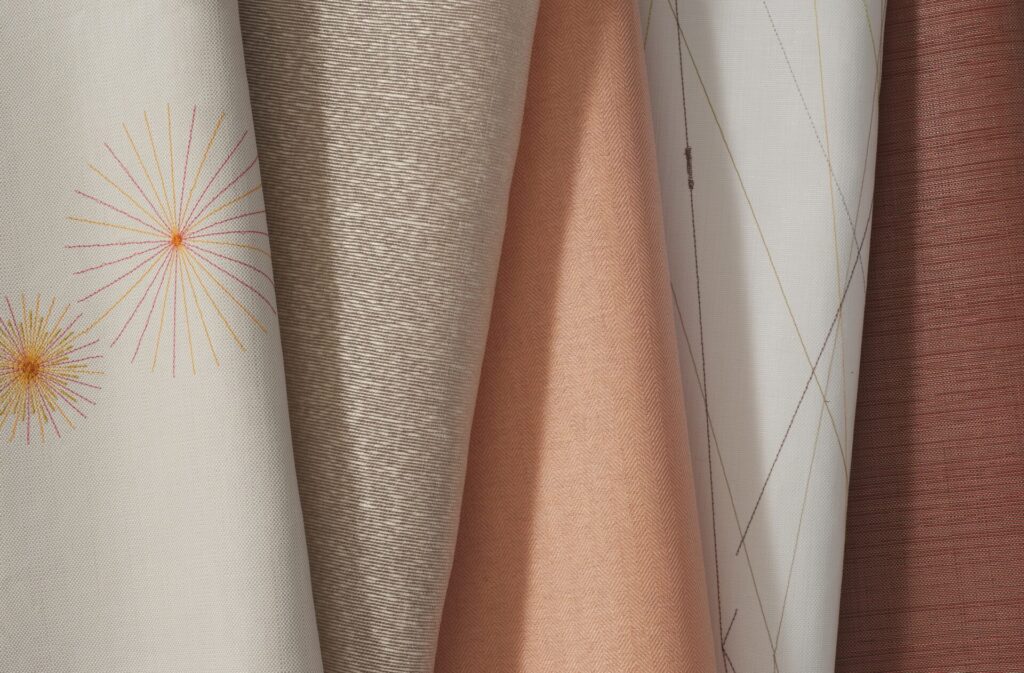 Close-up of Carnegie Crush commercial textiles showing embroidered, woven, textured, and performance upholstery and wallcovering fabrics in warm neutral tones.