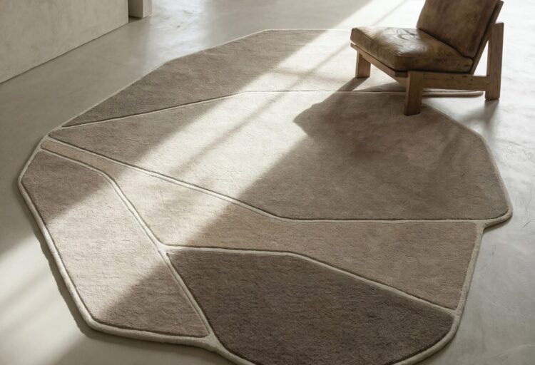 Hand-tufted Reef organic shaped rug by Carpet Edition with rounded geometric sections in varied pile heights, shown beneath a lounge chair in a minimalist interior.