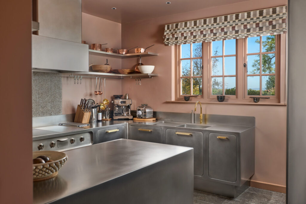 Wide view of the Abimis Ego stainless steel kitchen with seamless steel worktops, integrated appliances, brass faucet, and custom cabinetry in a London residence.