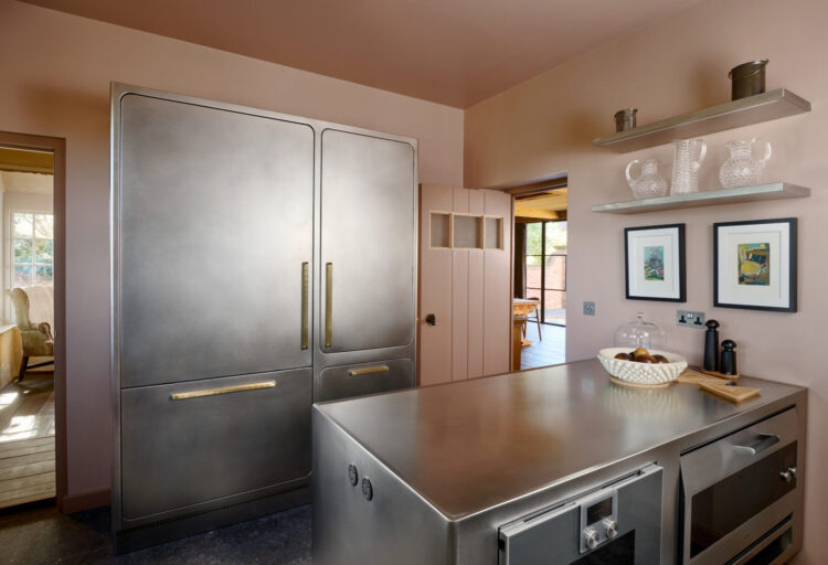 Abimis Ego stainless steel kitchen with seamless cabinetry, integrated refrigerator, brass handles, and hand-finished AISI 304 steel island in a converted London home.