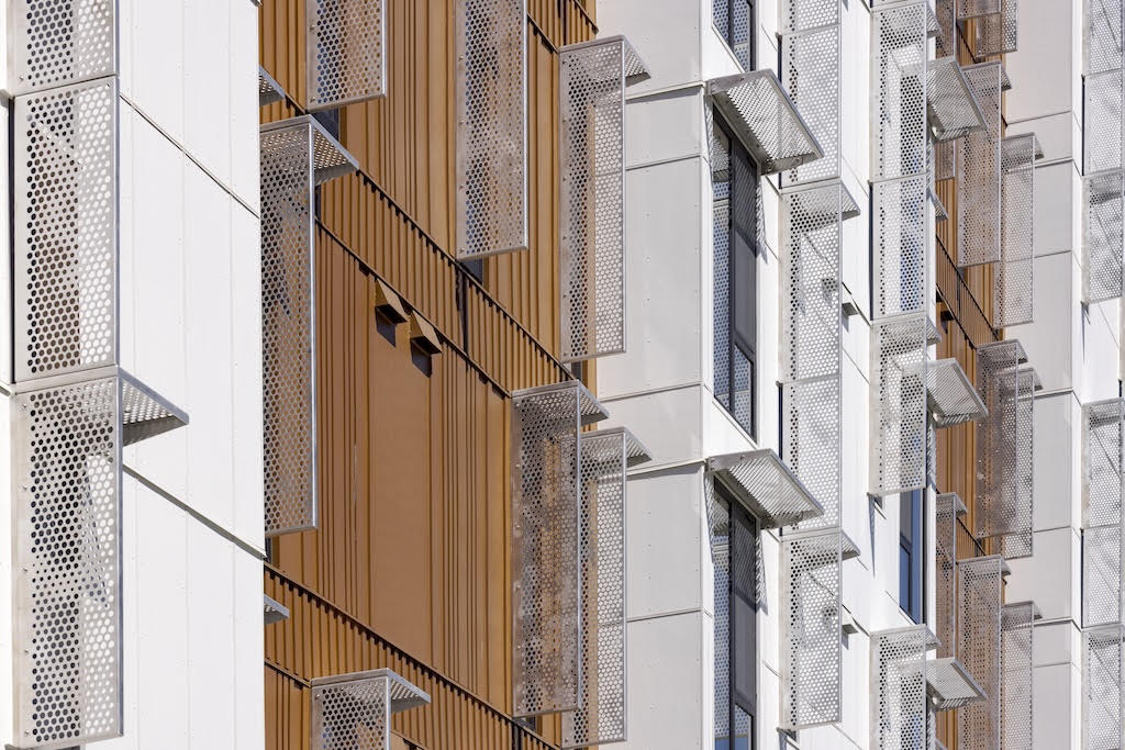 Architectural sunshades in perforated aluminum mounted directly to a white and bronze multifamily façade without visible brackets.