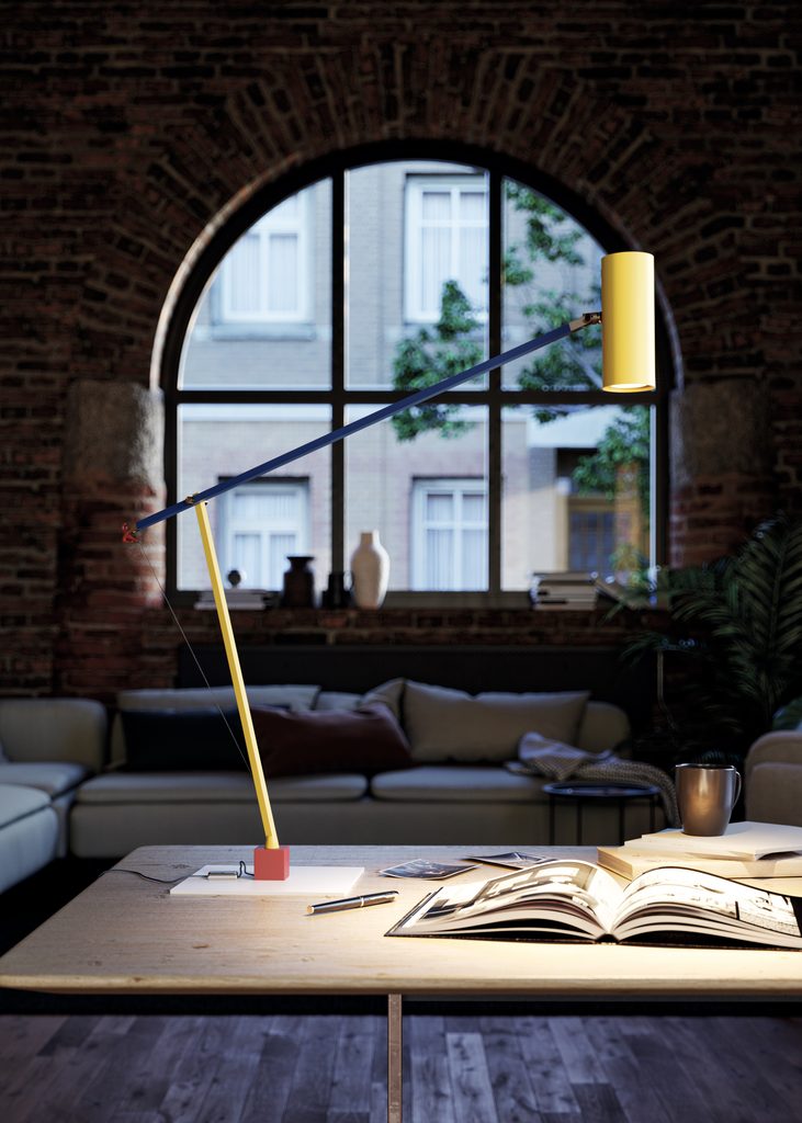Ettorino table lamp provides colorful lighting over an open book, with a blue arm, yellow stem and shade, and a small red dancing figure.
