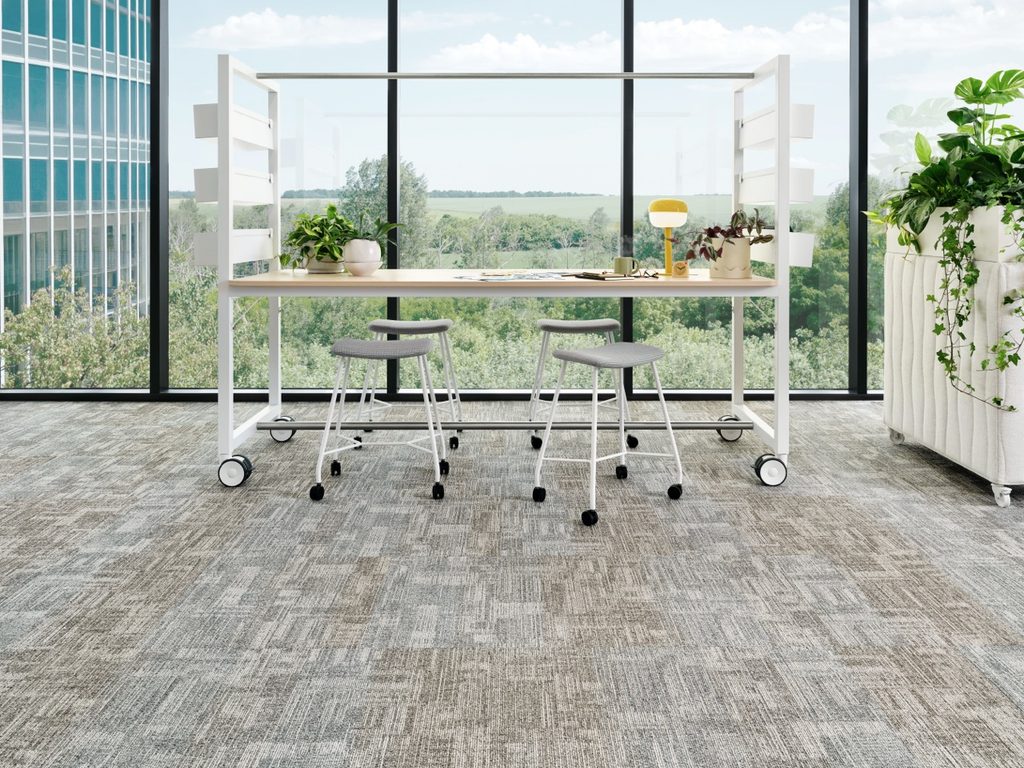 Shaw Contract textured carpet tile in gray and sand tones beneath a white rolling worktable and stools.