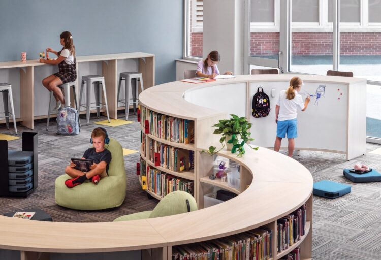 HON education furniture with curved Storyline bookcases, pale green lounge chairs, and whiteboard panels in a school library.