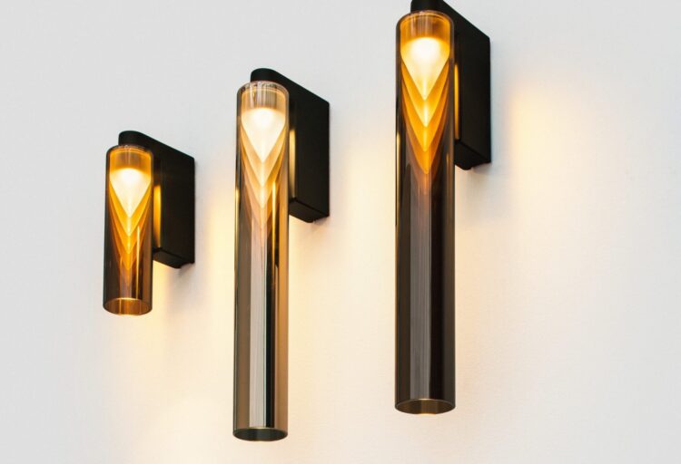 Penta Iconica glass wall sconce in three illuminated versions, with glowing cones reflected inside cylindrical shades on dark brackets.
