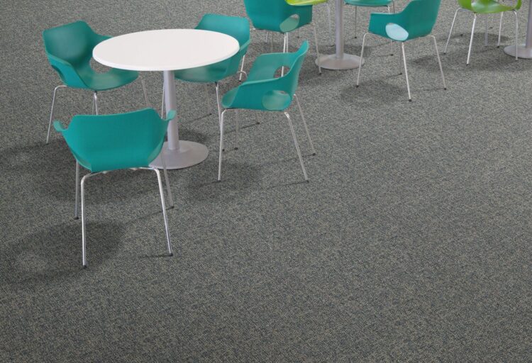 J+J Flooring Ume textile composite flooring beneath white café tables and teal and lime green chairs.