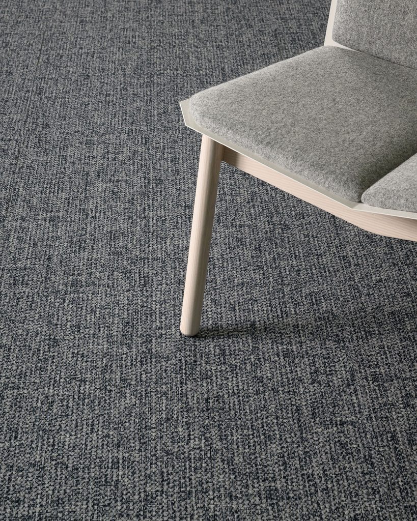 J+J Flooring Ume textile composite flooring with a fine gray weave beneath a wood-framed upholstered chair.