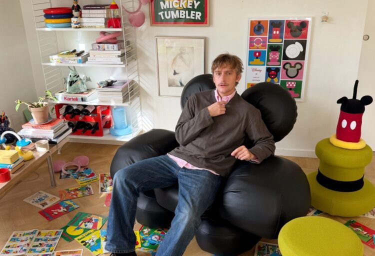 Person seated in the black Mickey Sofa amid Disney comics, posters and playful furniture by Gustaf Westman.
