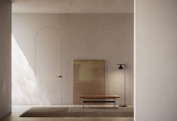 VIVA V0 Arco frameless arched door flush with a beige plaster wall, with a black lever handle beside a bench and floor lamp.