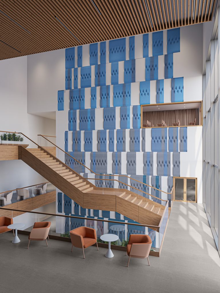 Blue and gray Xorel Artform Taper acoustic wall tiles cover a tall atrium wall beside a wood staircase.